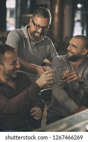 Cheerful Men Smiling, Looking At Each Other And Clinking Crystal Glasses. Friends Having Fun Together, Spending Time In Bar. Men Communicating, Drinking Alcohol As Brandy Or Whiskey.
