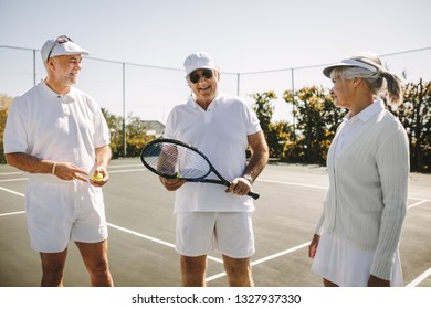 Cheerful men in tennis wear talking to a senior woman standing on a tennis court. Smiling old man standing with his playmates holding a tennis racket. - Powered by Shutterstock