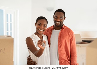 Cheerful Mid African Wife Holding New House Keys With Husband. Portrait Of Smiling Man Embracing Beautiful Wife Holding Keys Of New House. Happy Mature Black Couple Relocating And Looking At Camera.