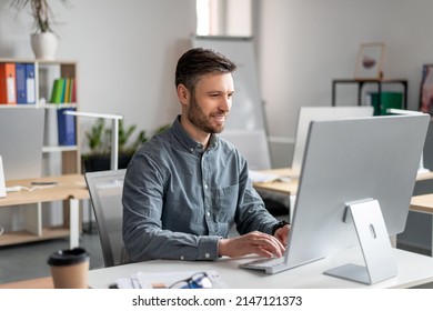 Empresario alegre de mediana edad sentado en la mesa de trabajo de la oficina, escribiendo en el teclado de la computadora, charlando con socios de negocios o trabajando en investigación de marketing