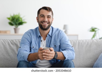 Cheerful middle aged caucasian man with beard in casual hold cup of drink look at camera at home interior, copy space. Rest, relaxation, take a break, free time and weekend, new normal due covid-19