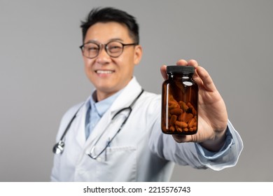 Cheerful Middle Aged Chinese Male Doctor In White Coat, Glasses Shows Jar Of Pills, Isolated On Blue Background, Studio, Close Up. Professional Recommendation, Treatment, Health Care And Medicine