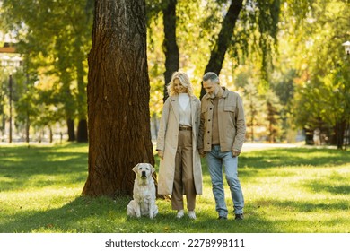 cheerful middle aged couple in casual attire walking out with labrador dog in green park during springtime - Powered by Shutterstock