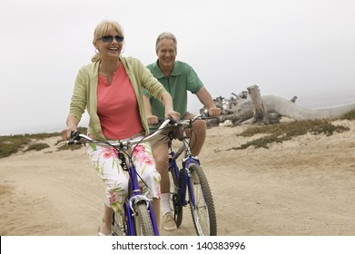 Cheerful Middle Aged Couple Riding Bicycles Along The Beach