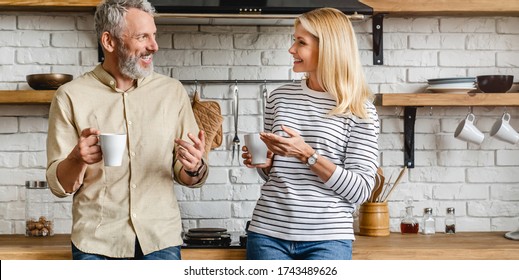 Cheerful Middle Aged Couple Talking On Kitchen While Drinking Coffee