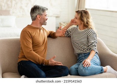 Cheerful Middle Aged Couple Talking And Flirting Enjoying Conversation Spending Time Together Sitting On Sofa At Home. Happy Marriage And Romantic Relationship Concept - Shutterstock ID 2159141563