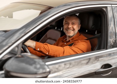 Cheerful middle aged man driving car, looking through open window and smiling at camera, European man enjoying car ride, side view - Powered by Shutterstock