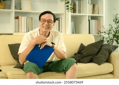 Cheerful middle aged man wearing glasses and casual clothed sitting on sofa in a cozy living room - Powered by Shutterstock