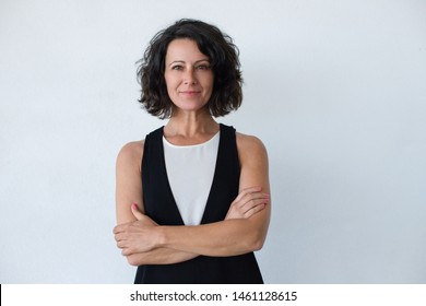 Cheerful middle aged woman with curly hair. Portrait of attractive brunette woman standing with crossed arms and smiling at camera isolated on grey background. Emotion concept - Powered by Shutterstock