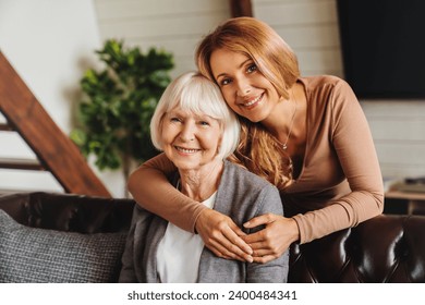 Cheerful middle aged woman embracing senior mother at home and looking at camera. Love and care. Family time and bonding concept. Assistance and support of elder generation - Powered by Shutterstock