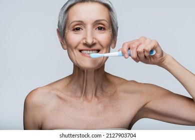 Cheerful Middle Aged Woman Holding Toothbrush And Brushing Teeth Isolated On Grey