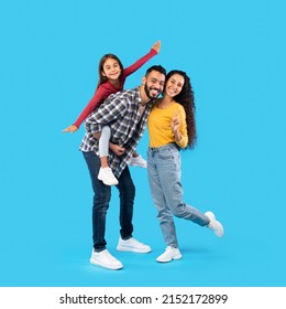 Cheerful Middle Eastern Family Having Fun Posing Together, Father Carrying His Daughter Piggyback Standing Over Blue Studio Background. Square Shot, Full Length - Shutterstock ID 2152172899