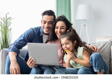 Cheerful Middle Eastern Family Shopping Online With Laptop And Credit Card At Home, Happy Arab Parents And Their Little Daughter Relaxing On Couch With Computer, Purchasing In Internet, Closeup