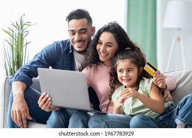 Cheerful Middle Eastern Family Of Three With Laptop And Credit Card At Home Making Online Hotel Reservation Or Shopping In Internet While Relaxing Together On Couch With Computer, Closeup Shot