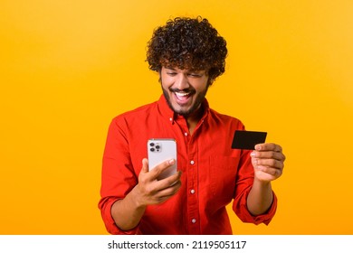 Cheerful middle eastern guy is using smartphone and credit card for shopping online. Happy man is ordering food online, male paying for long-awaited purchase on the mobile phone, isolated on orange - Shutterstock ID 2119505117