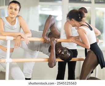 Cheerful middle-aged African American male ballet dancer playfully goofing around by barre, making fellow dancers laugh during break in rehearsal in sunlit choreography studio - Powered by Shutterstock