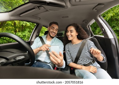 Cheerful Middle-eastern Guy Driver Travelling With His Beautiful Long-haired Girlfriend By Nice Automobile, Setting Gps On Cellphone, Couple Looking At Smartphone Screen, Shot From Car Dashboard