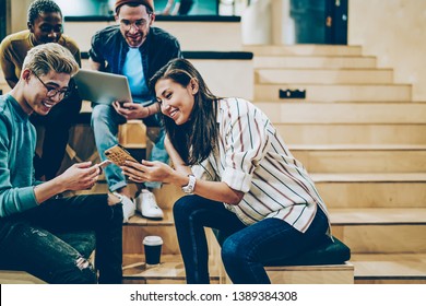 Cheerful millenial woman showing latest feed from social networks to group of multiracial friends, happy crew of male and female colleagues spending free time in college talking and using gadgets