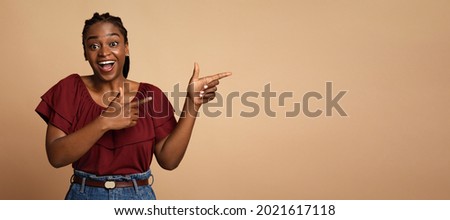 Cheerful millennial black lady posing over colorful background, pointing at copy space and smiling. Beautiful young african american woman showing text or advertisement on beige, panorama