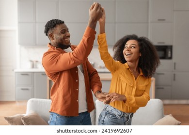 Cheerful millennial black spouses having fun together dancing to music in modern kitchen interior, smiling to each other. Couple having date or party. Relationship and romance concept - Powered by Shutterstock