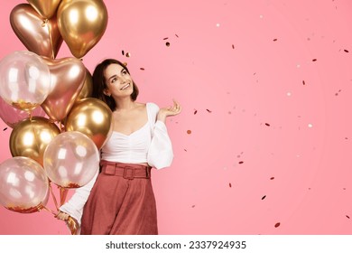 Cheerful millennial caucasian brunette lady with many balloons enjoy confetti, isolated on pink background, studio. Ad and offer, lifestyle, holiday celebration, birthday party and fun - Powered by Shutterstock