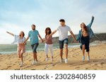 Cheerful millennial european and arab friends have fun, enjoy free time, jump and run on ocean beach, summer party, full length. Walk, vacation together, holiday and trip outdoor
