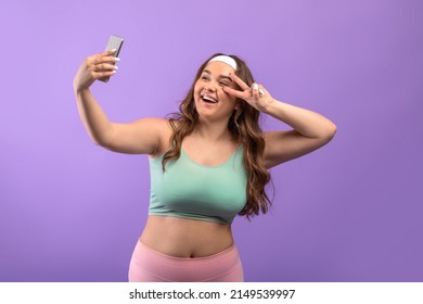 Cheerful Millennial European Plus Size Lady In Sportswear Taking Selfie On Phone And Shooting Livestream, Isolated On Purple Background, Studio. Photo, App For Fitness Blog And Website, Modern Tech