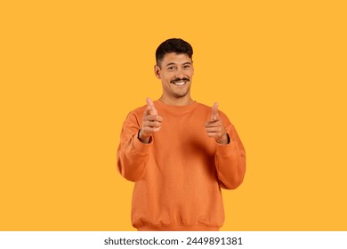 Cheerful millennial guy with a moustache smiling and giving thumbs up, posed on a funny isolated vibrant orange background