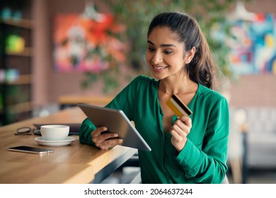 Cheerful millennial indian lady banking online, using digital tablet and credit card at cafe, young woman buying clothes or cosmetics on Internet, using shopping mobile application on pad