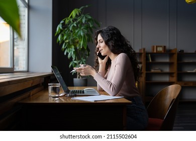 Cheerful Millennial Woman Freelance Financial Advisor Sit At Table Look And Point At Computer Screen Discuss Project Plan On Mobile Phone With Customer Suggest Solution For Business Issues Distantly