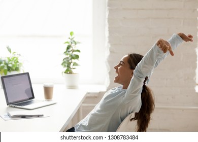 Cheerful mixed race woman sitting at workplace on chair bending stretching raising hands up, feels happy got a long-awaited post winning online lottery or accomplishing working day before vacation