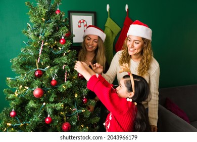 Cheerful Mixed-race Family Decorating The Christmas Tree At Home. Gay Moms And Daughter Celebrating Together 