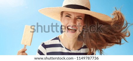 cheerful modern woman in straw hat against blue sky with ice cream on a stick
