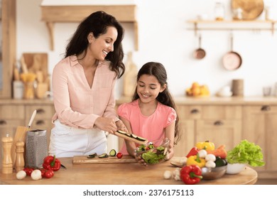 Cheerful mom and daughter kid joyfully making salad from fresh organic vegetables in modern kitchen interior, adding cut ingredients to bowl. Healthy eating habits, family nutrition - Powered by Shutterstock