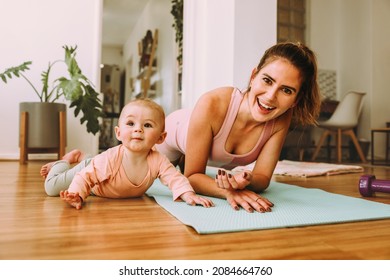 Cheerful mom doing plan exercises with her baby at home. Happy young mom working out with her baby on an exercise mat. New mom bonding with her baby during her post-natal fitness routine.