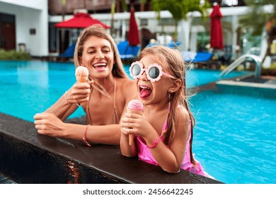 Cheerful mother and daughter enjoy ice cream by poolside. Little girl in pink swimsuit, goggles eats dessert, laughs. Mom joins fun on sunny day. Family pool time, sweet treat moment captured. - Powered by Shutterstock