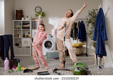 Cheerful mother and daughter spend time together while cleaning house. Woman and child perform household chores in laundry bathroom clean floor mop and sweeping brush in hands dancing fooling around.