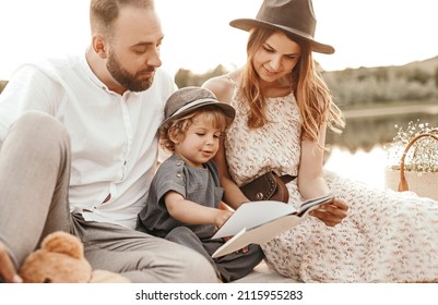 Cheerful mother and father reading fairytale with adorable curious child while sitting on pier near lake and spending weekend together in summer