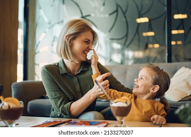 Cheerful mother and her daughter having fun with whipped cream while eating mousse together. - Powered by Shutterstock