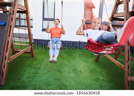 Cheerful mother and her daughter having fun on swings at the park. Mother and her child fooling around together. Stock photo
