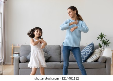 Iloinen äiti pieni tytär seisoo olohuoneessa kotona liikuttaen tanssia lempikappaleeseen yhdessä. Lapsi pitää hauskaa vanhempi sisko lastenhoitaja tai rakastava äiti aktiivinen vapaa-ajan ja elämäntavan käsite