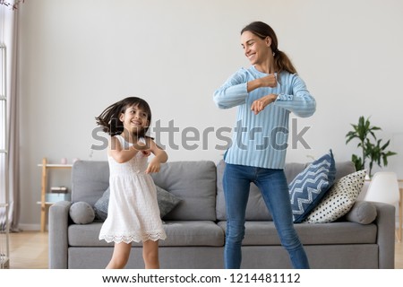 Cheerful mother little daughter standing in living room at home moving dancing to favourite song together. Child have fun with elder sister nanny or loving mother active leisure and lifestyle concept