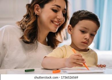 cheerful mother looking at adorable son drawing and felt  tip pen