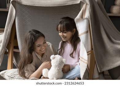 Cheerful mother and playful child playing in toy handmade tent together, resting under hanging blanket, smiling, laughing, chatting, enjoying family playtime activity, leisure - Powered by Shutterstock