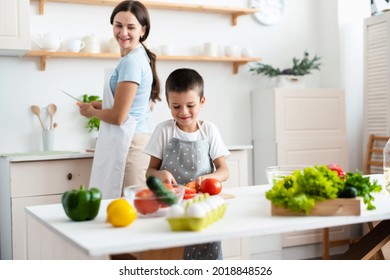 Cheerful mother proud her self-dependent son. Child unaided is cooking salad at kittchen. Healthy food concept. - Powered by Shutterstock