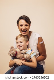 Cheerful mother and son after vaccination on brown background. Woman holding her son with a teddybear.