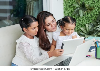 Cheerful mother and two girls sitting at table in backyard and watching animated movie on tablet computer