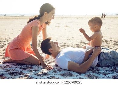 Cheerful Multi Ethnic Family Have A Rest On A Sea Shore. Young Family, Man Woman And Little Son Enjoy Picnic, Summer Outdoor, Good Weather