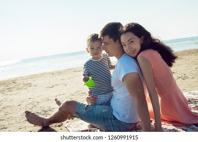 Cheerful Multi Ethnic Family Have A Rest On A Sea Shore. Young Family, Man Woman And Little Son Enjoy Picnic, Summer Outdoor, Good Weather