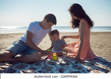 Cheerful Multi Ethnic Family Have A Rest On A Sea Shore. Young Family, Man Woman And Little Son Enjoy Picnic, Summer Outdoor, Good Weather